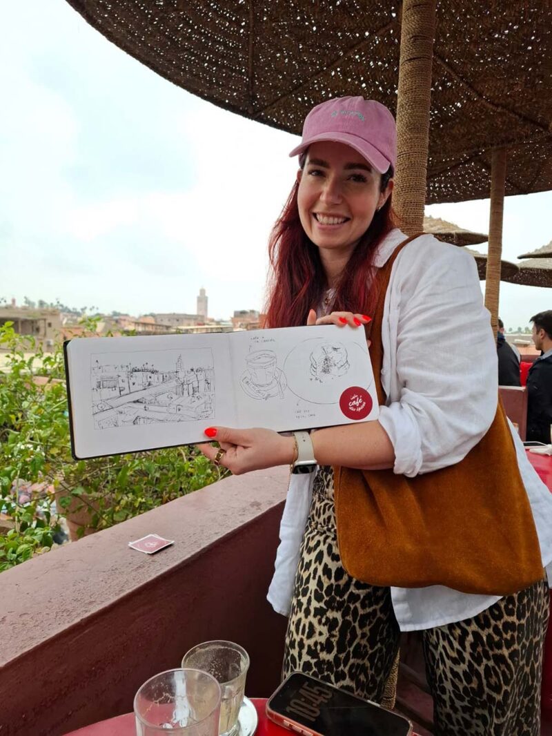 Deelnemer laat haar getekende travel journal zien op het dakterras