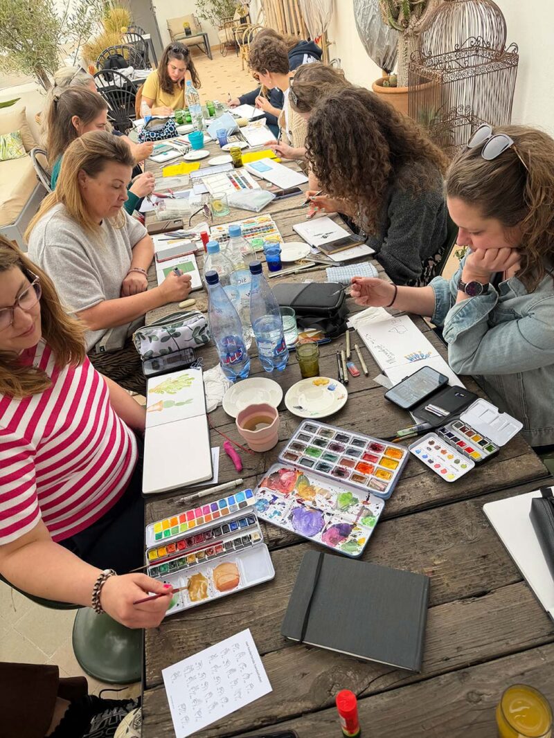 De groep aan tafel met verfdozen en schetsboeken